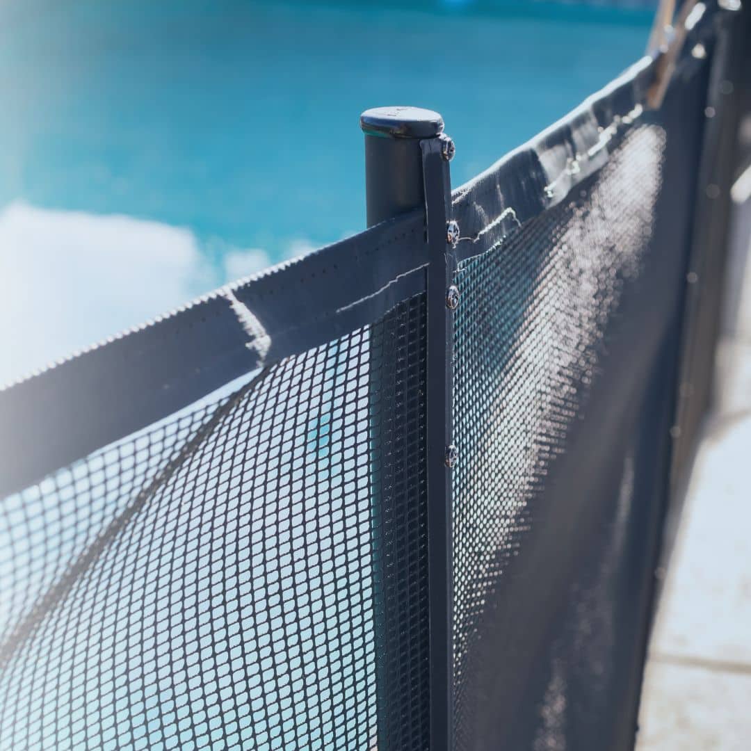 Black mesh pool safety fence and post installed beside a backyard pool