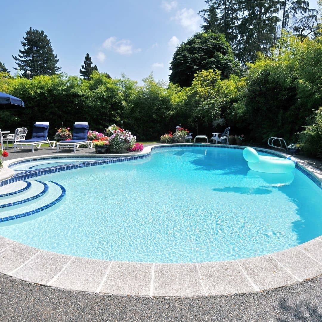 Backyard in-ground residential swimming pool with clear blue water, a concrete deck, and patio furniture, ready for a professional pool inspection.